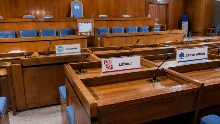 Swindon Borough Council chamber with desks displaying Reform UK, Labour and Conservative nameplates ahead of a Finance Recovery Board meeting.