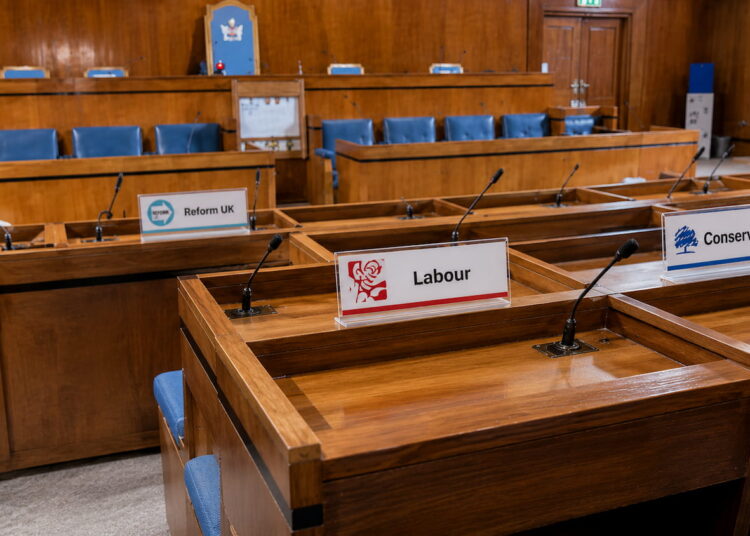 Swindon Borough Council chamber with desks displaying Reform UK, Labour and Conservative nameplates ahead of a Finance Recovery Board meeting.